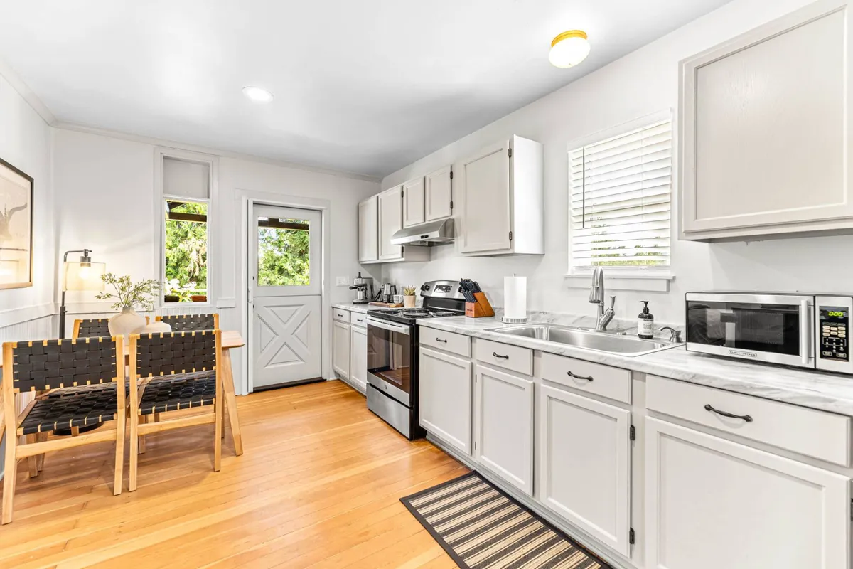 A sunlit kitchen island with dining chairs and a window offering a pleasant view. The scene is set for shared meals or casual gatherings, with the warmth of natural light enhancing the inviting mood.