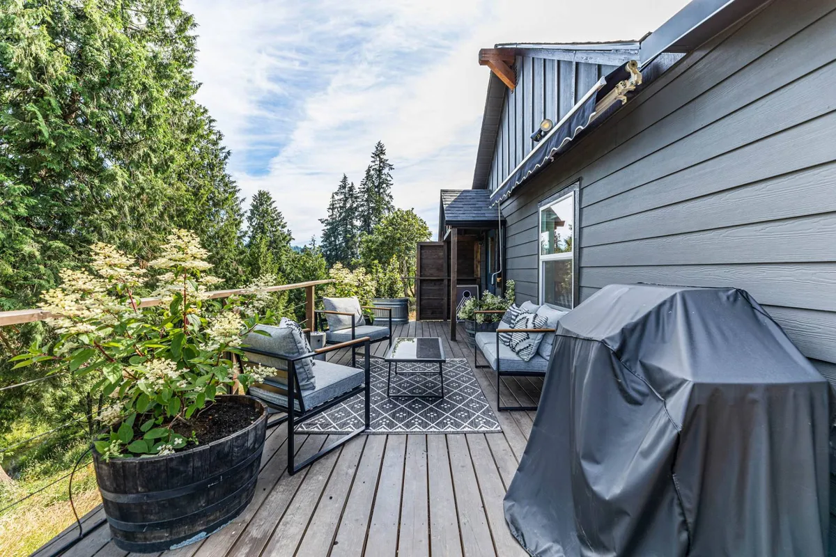 An inviting outdoor seating area complete with a grill and planters. The area is designed for al fresco dining and socializing, with comfortable seating and natural greenery creating a relaxed, enjoyable space. The deck is clearly a hub for gatherings and outdoor meals.