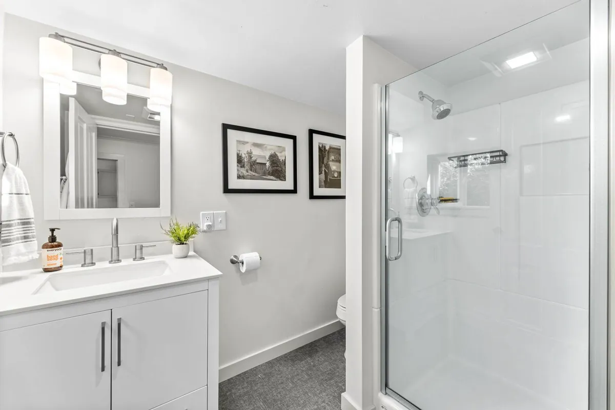 A bright, spa-inspired bathroom featuring a vanity with sink, framed artwork, and a glass shower enclosure. The space is calm and inviting, with natural light enhancing the tranquil atmosphere and modern amenities evident throughout.