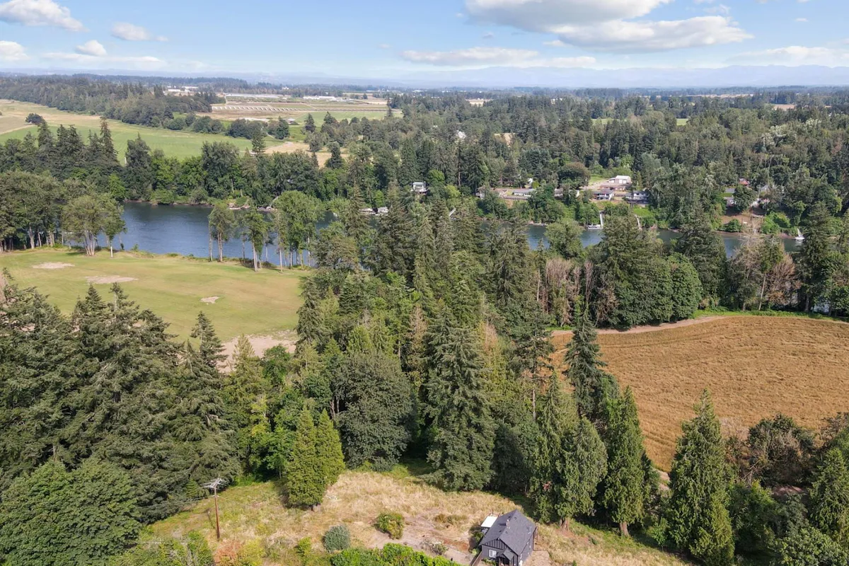 This image features a serene view of the Willamette River framed by forest and open fields, with distant houses dotting the landscape. The riverbank is ideal for hiking, fishing, picnicking, and nature walks. The scene is suffused with soft sunset light, enhancing the tranquil mood and evoking a sense of peaceful rural exploration.
