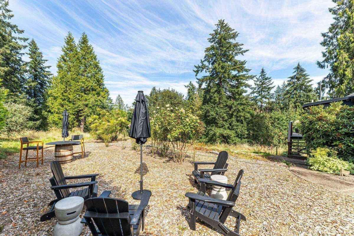 A peaceful outdoor deck scene featuring Adirondack chairs around a small table with an umbrella overhead. The deck is nestled among mature trees, providing a sense of privacy and immersion in nature. Dappled sunlight filters through the leaves, and the overall atmosphere is tranquil and inviting.
