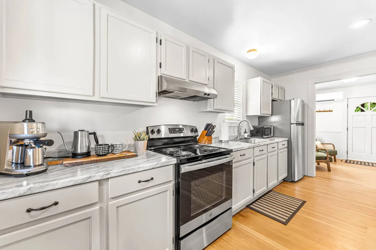 A bright, modern kitchen featuring stainless steel appliances, white cabinets, a marble countertop, and wooden flooring. The layout is open and inviting, perfect for both everyday cooking and entertaining guests.