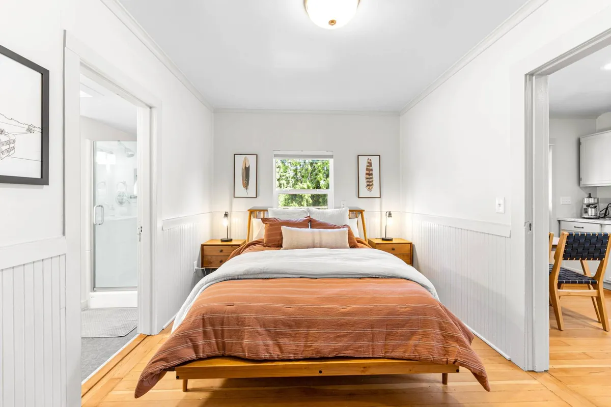 A second bedroom view with a comfortable bed, nightstands, a window letting in sunlight, and tasteful artwork. The overall mood is cozy and peaceful, inviting moments of relaxation and reading.